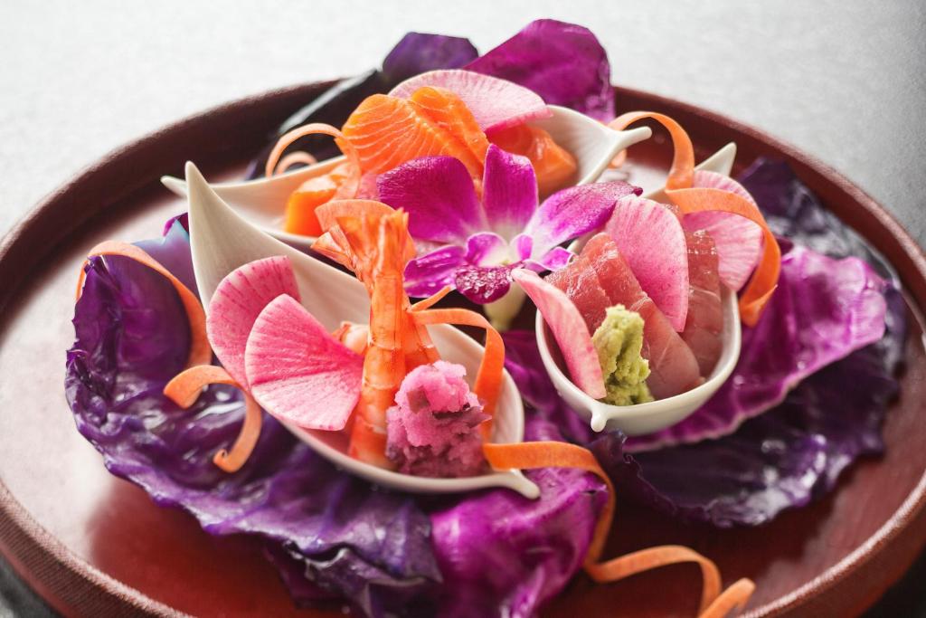 une assiette de nourriture avec des fleurs violettes et oranges dans l'établissement Ryokan KANADE, à Kyoto 37 autres photos