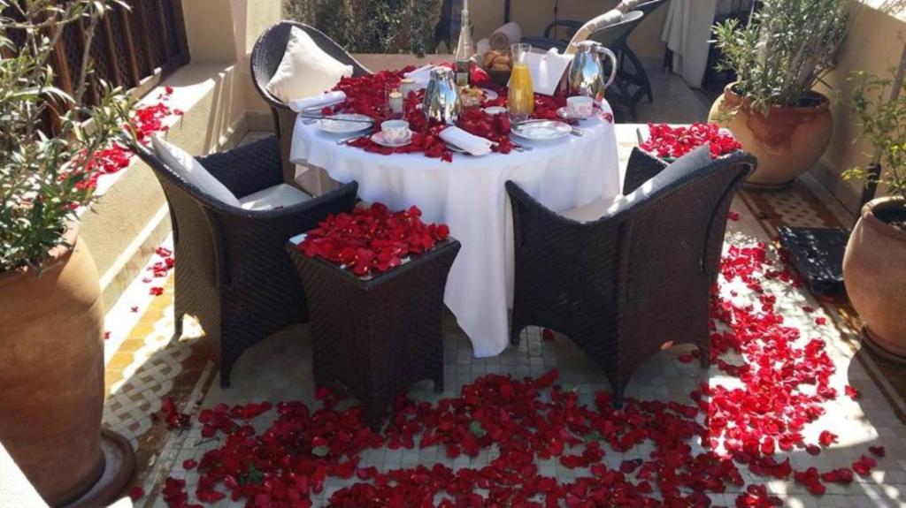 une table avec un chiffon de table blanc et des fleurs rouges dans l'établissement Riad ILayka, à Marrakech
