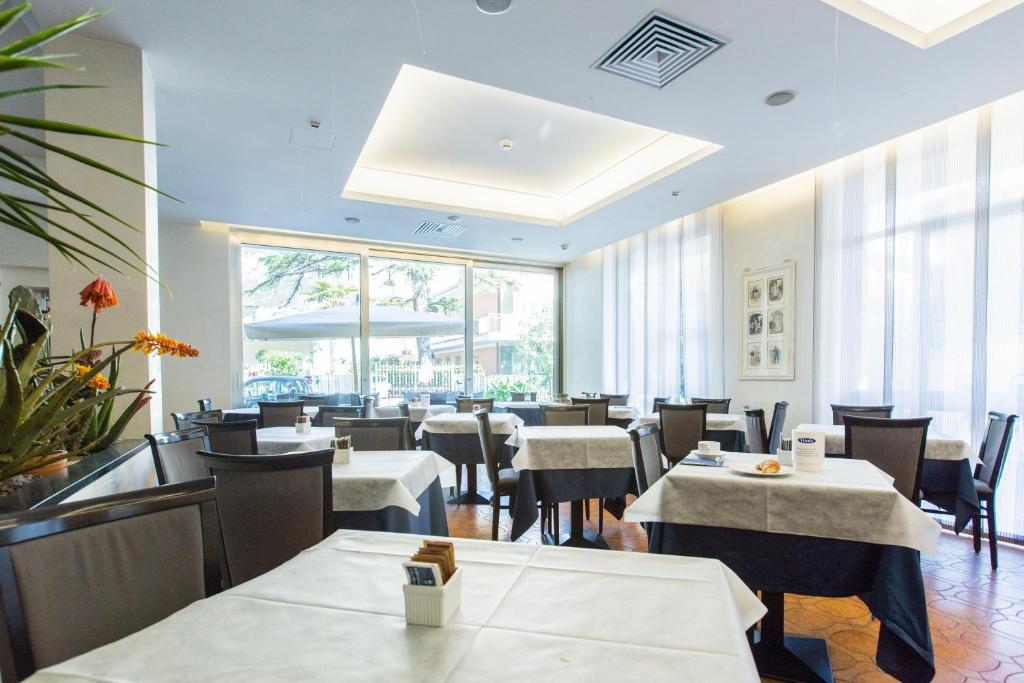 une salle à manger avec des tables et des chaises blanches et des fenêtres dans l'établissement Nautilus, à Riccione