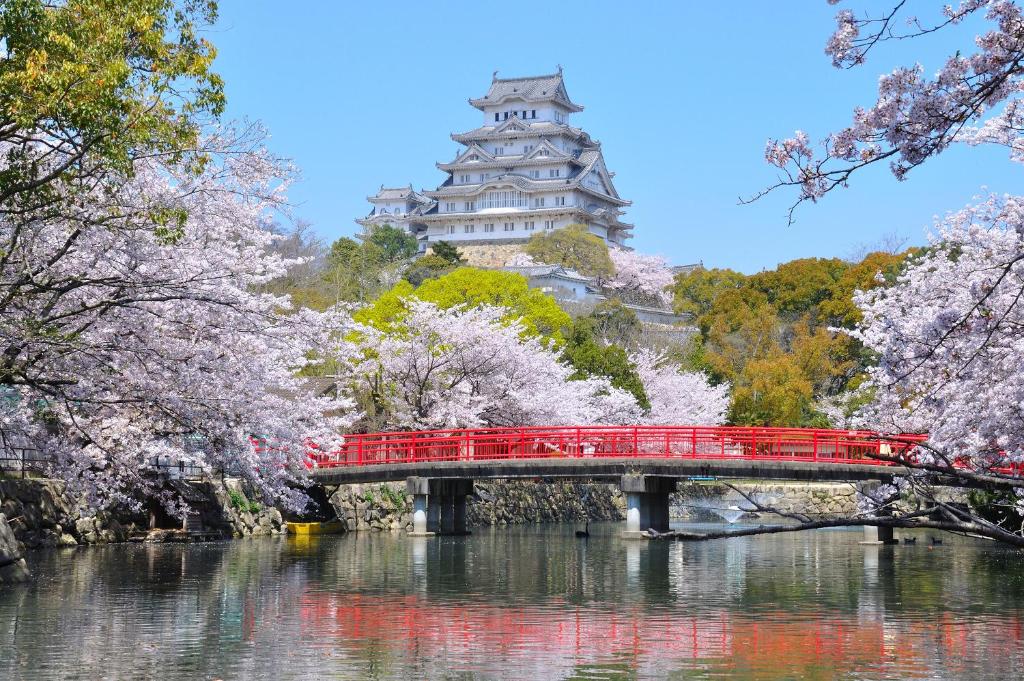 un pont rouge sur une rivière avec un château en arrière-plan dans l'établissement Himeji Park Hotel (Adult Only), à Himeji
