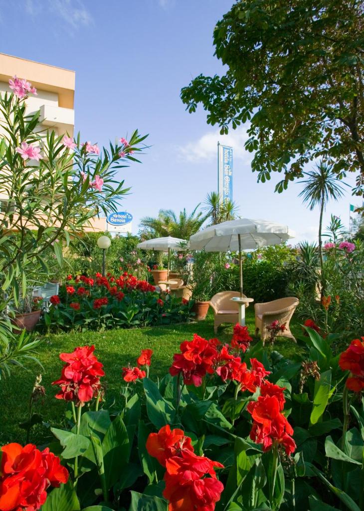 un jardin avec des fleurs rouges, des chaises et des parasols dans l'établissement San Giorgio Savoia, à Bellaria-Igea Marina