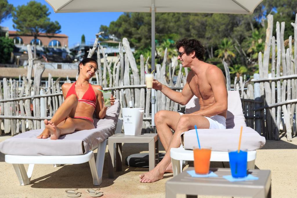 un homme et une femme assis sur des chaises de plage sous un parasol dans l'établissement Frantheor Fréjus 5 étoiles, à Fréjus