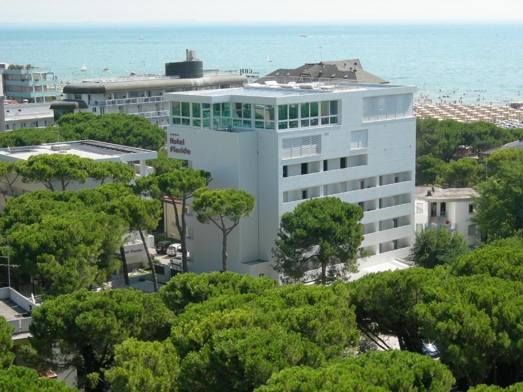 Un bâtiment blanc avec des arbres en face de l'océan dans l'établissement Hotel Florida, à Lignano Sabbiadoro