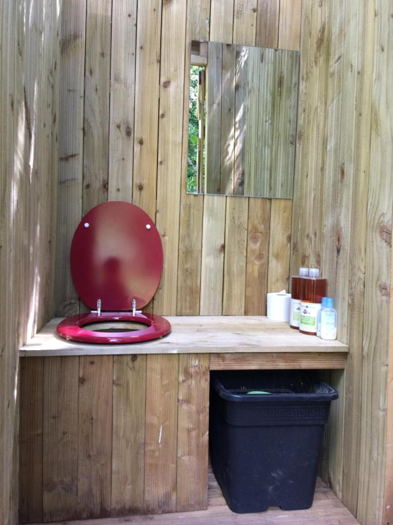 La salle de bains est pourvue de toilettes rouges dans un mur en bois. dans l'établissement Tipis nature, à Gavarnie