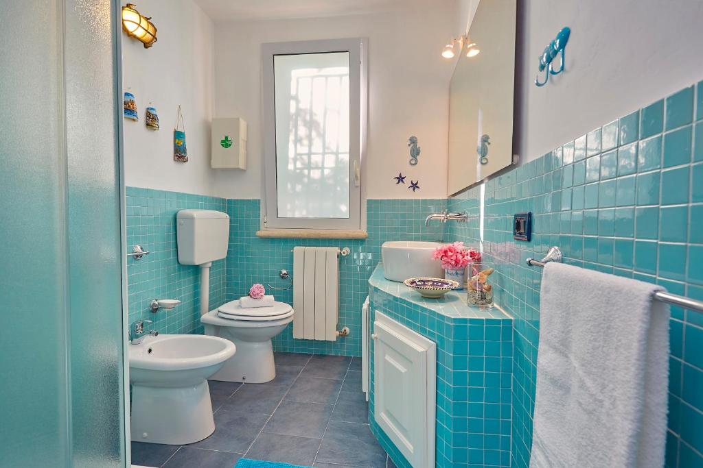 La salle de bains est pourvue de carrelage bleu, de toilettes et d'un lavabo. dans l'établissement Villa Ginestra - Scopello-Villas, à Scopello