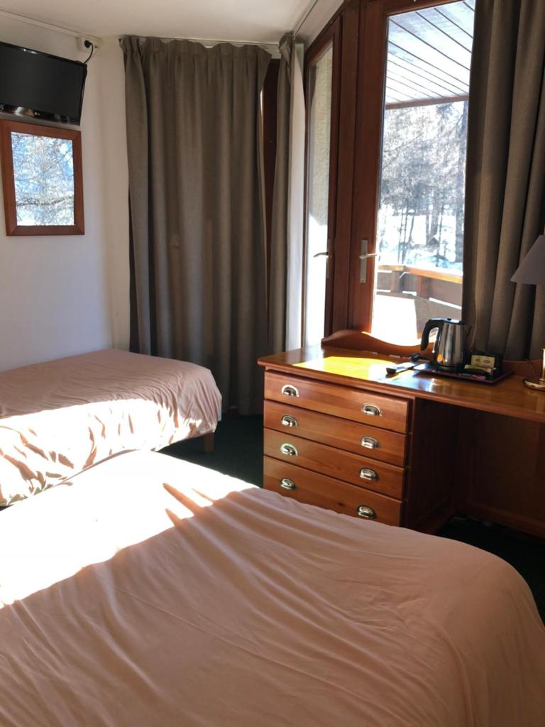 une chambre avec deux lits et une commode et une fenêtre dans l'établissement Hôtel Les Trappeurs, aux Orres