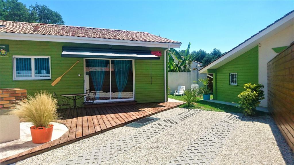 une maison verte avec une terrasse en bois devant dans l'établissement Gîte avec piscine et espace bien-être partagés entre Bordeaux et Lacanau océan, à Brach