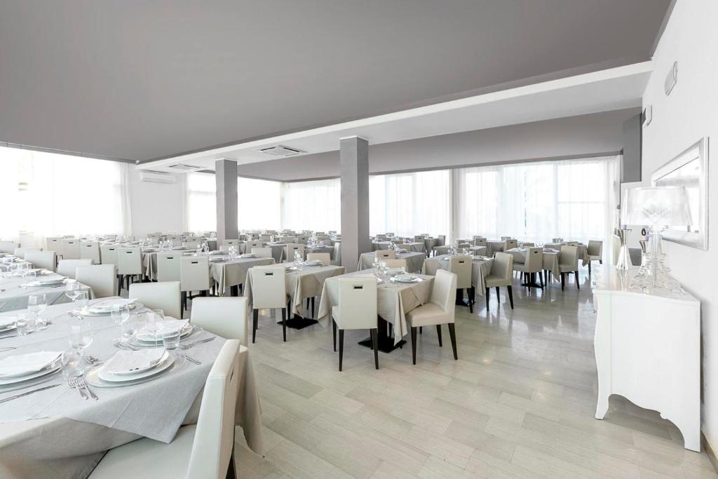 une grande salle à manger avec des tables et des chaises blanches dans l'établissement Hotel Excelsior, à Alba Adriatica