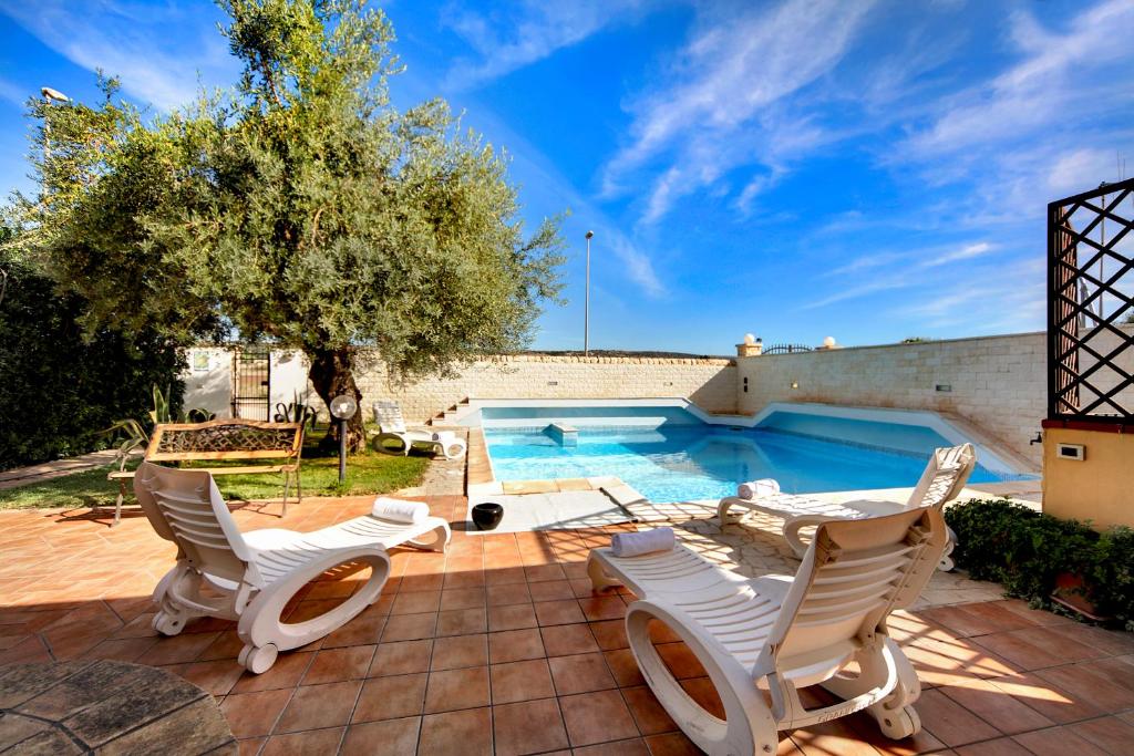 une terrasse avec des chaises blanches et une piscine dans l'établissement Villa dell'Ulivo, à Marina di Ragusa