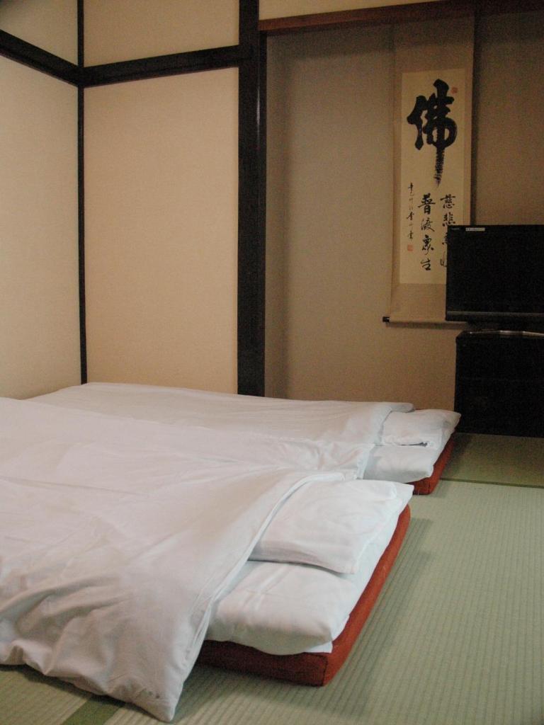 Cette chambre comprend un lit avec des draps blancs. dans l'établissement くさつのお宿 清重館 Kiyoshigekan 素泊りの宿, à Kusatsu