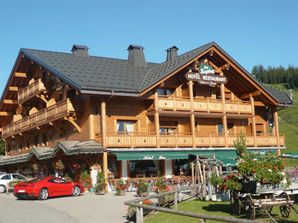 un grand bâtiment en bois avec une voiture rouge garée devant dans l'établissement Hôtel Restaurant "Les Sapins" Wellness & Gourmet, à Manigod