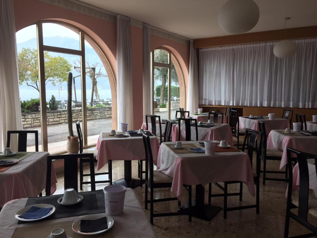 une salle à manger avec tables, chaises et fenêtres dans l'établissement Piccolo Hotel Direkt am See, à Brenzone
