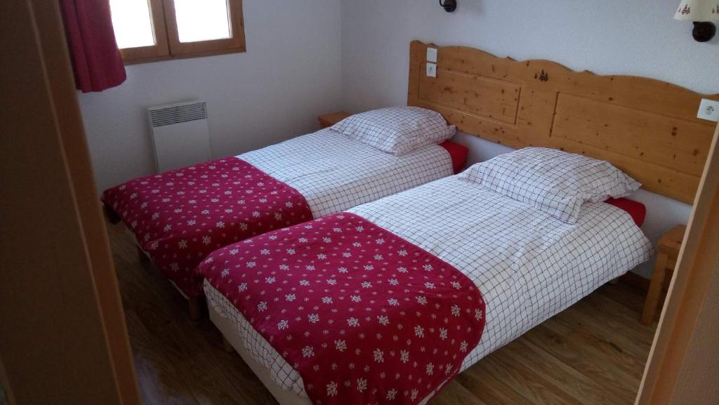 Cette chambre comprend 2 lits avec des draps rouges et blancs. dans l'établissement Le Hameau des Ecrins Station 1800, à Puy-Saint-Vincent
