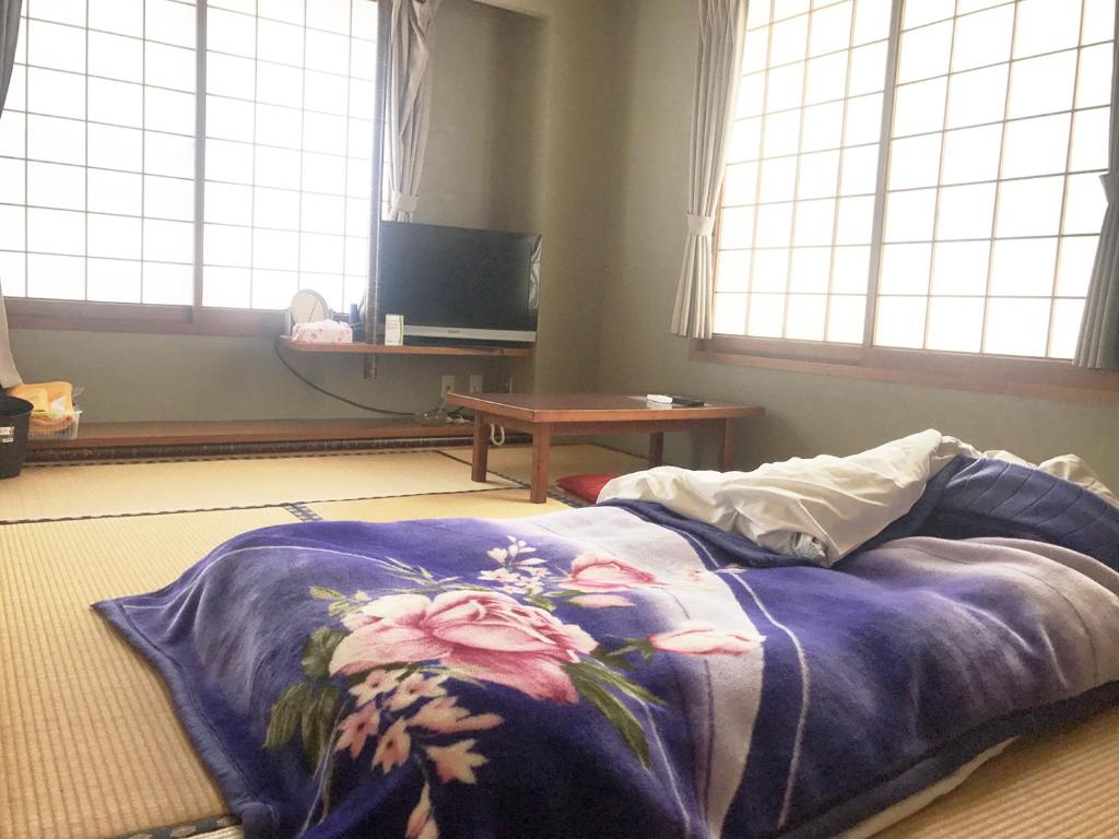 - un lit avec une couverture bleue sur le sol et des fenêtres dans l'établissement business ryokan haniwa, à Saito