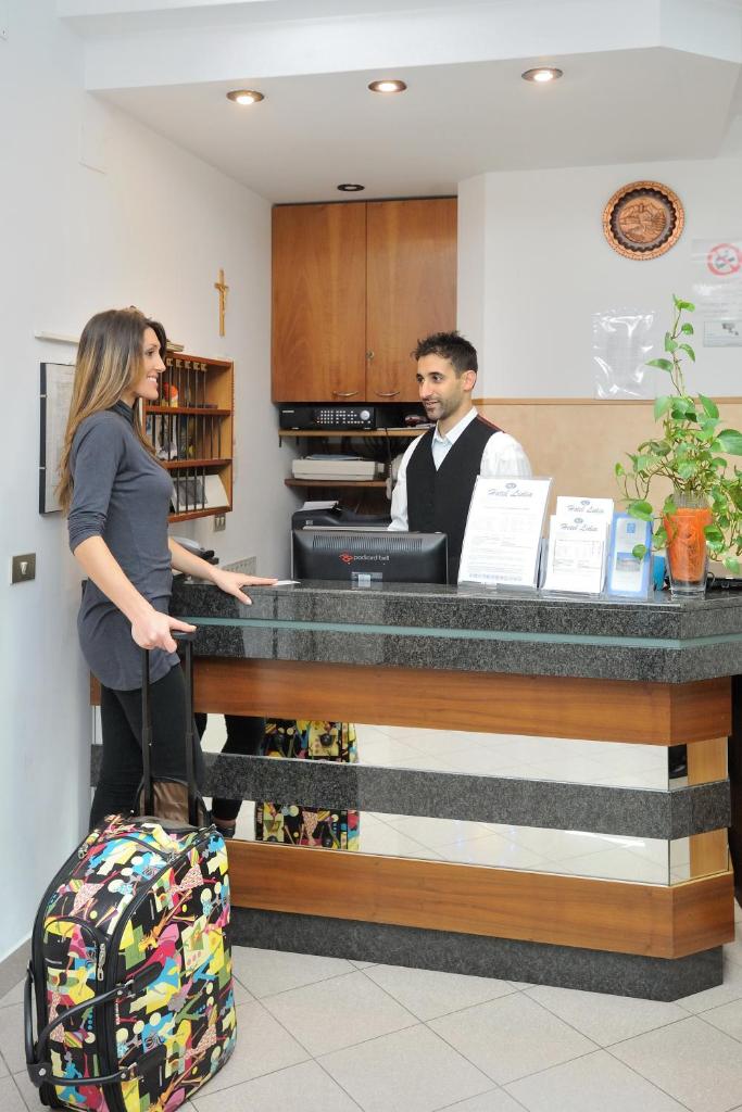 une femme avec une valise debout au comptoir avec un homme dans l'établissement Hotel Lidia, à Alba Adriatica