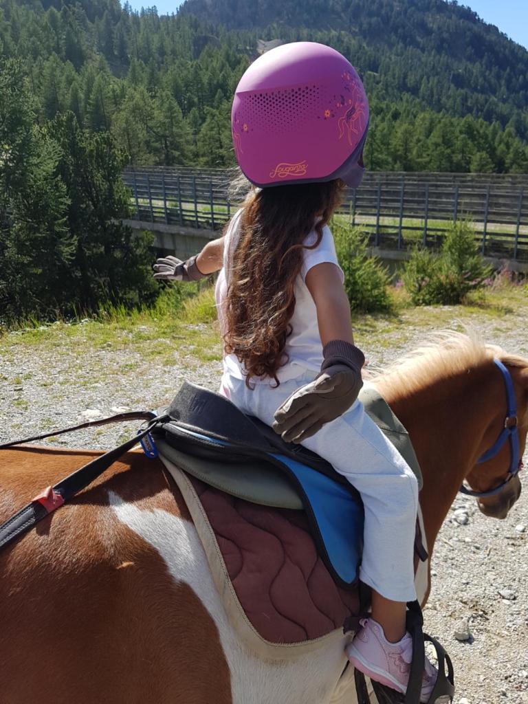Une petite fille qui fait de l'équitation à l'arrière d'un cheval dans l'établissement Front de Neige Isola 2000, à Isola 2000