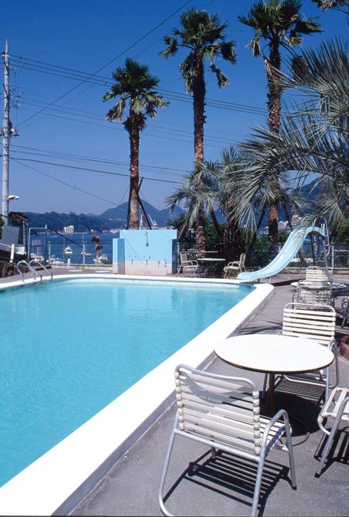 une piscine avec une table, des chaises et des palmiers dans l'établissement Hotel Yamadaya, à Shimoda