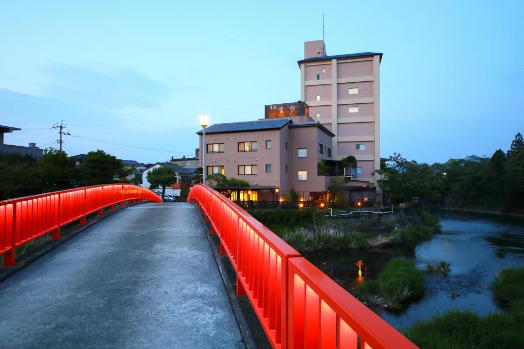 un pont rouge sur une rivière avec un bâtiment dans l'établissement Onyado Takasago, à Ureshino