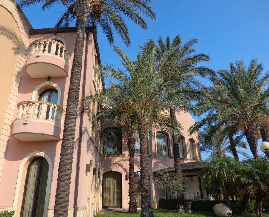 un bâtiment rose avec des palmiers devant lui dans l'établissement TH Le Castella - Baia degli Dei Village, à Le Castella