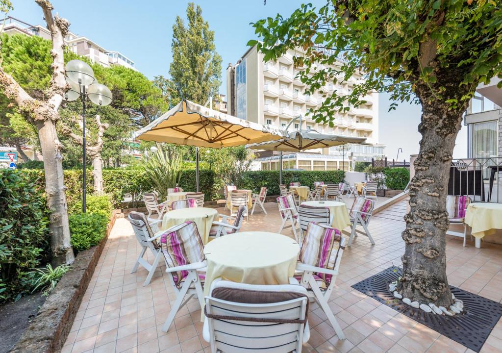 un patio avec des tables et des chaises sous un arbre dans l'établissement Hotel Fenice Gluten Free, à Milano Marittima