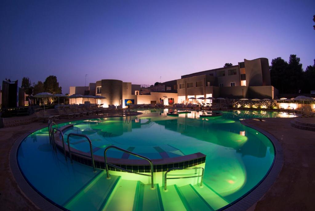 une grande piscine avec des lumières vertes dans un complexe hôtelier la nuit dans l'établissement Futura Club Spiagge Bianche, à Fontane Bianche