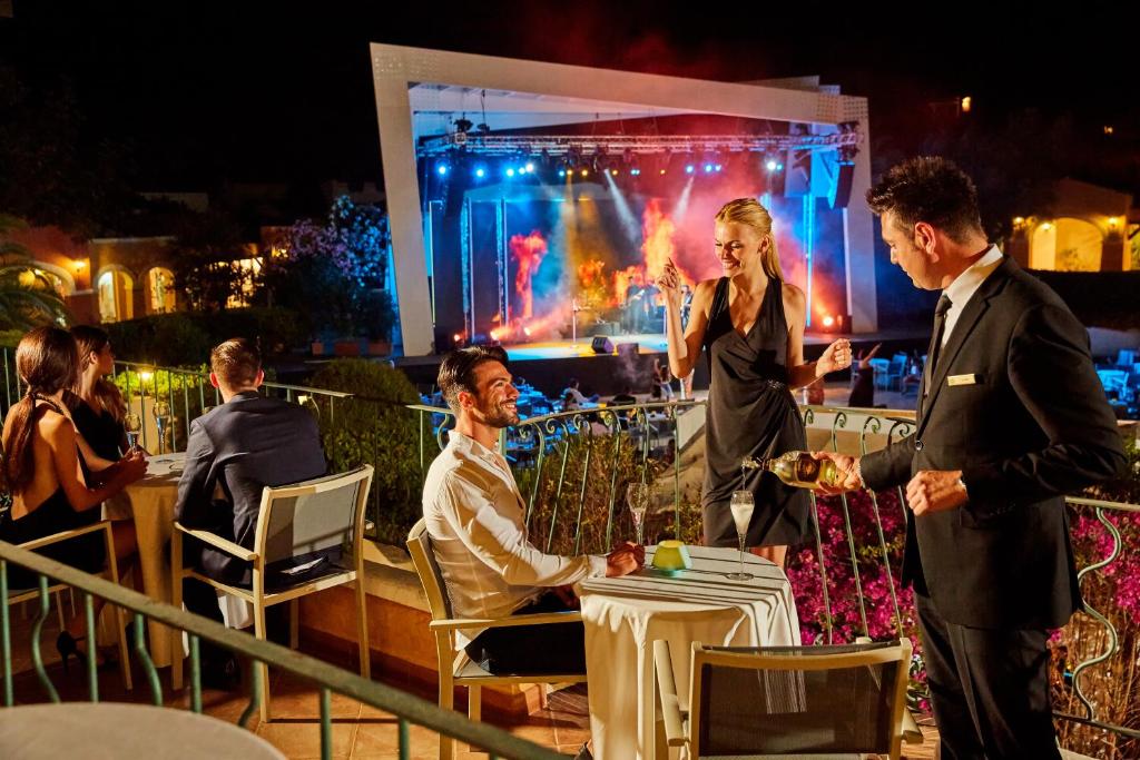 un homme et une femme debout à une table devant une scène dans l'établissement Forte Village Resort - Le Palme, à Santa Margherita di Pula