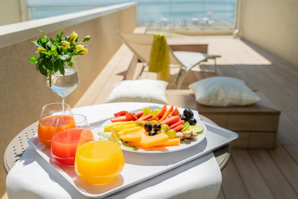 une assiette de fruits et légumes sur une table avec des verres de jus d'orange dans l'établissement Hotel Elite, à Caorle