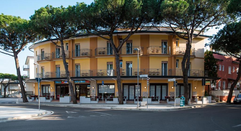 un bâtiment jaune avec des arbres devant lui dans l'établissement Hotel Residence Mara, à Lido di Jesolo