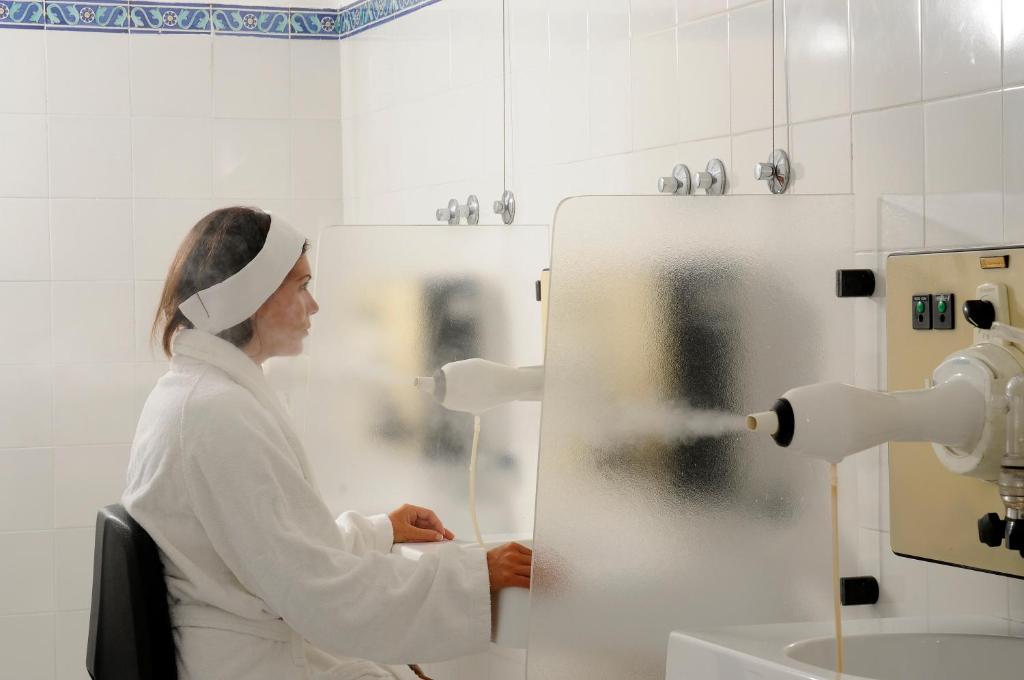 une femme assise dans une chaise et regardant un robinet dans une salle de bains dans l'établissement Hotel La Villarosa Terme, à Ischia