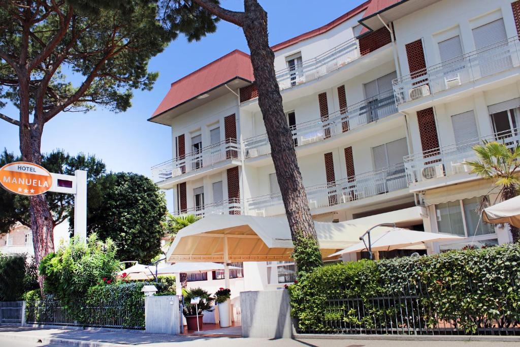 un grand bâtiment blanc avec des parasols en face de celui-ci dans l'établissement Hotel Manuela, à Cervia