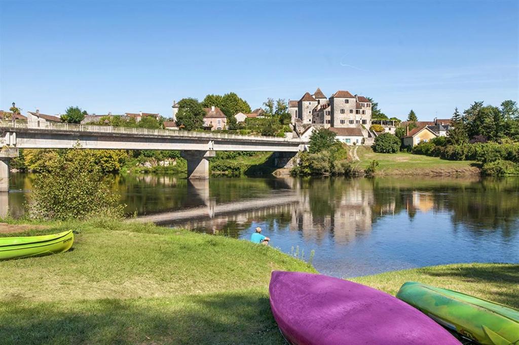 un pont sur une rivière avec des bateaux sur l'herbe dans l'établissement Camping les Borgnes Saint-Sozy, à Saint-Sozy