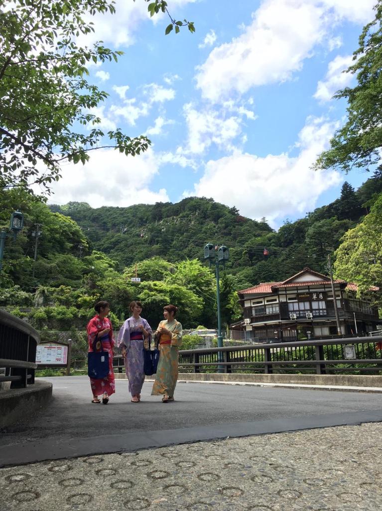 Trois femmes marchant dans une rue avec des montagnes en arrière-plan dans l'établissement Shikanoyu Hotel, à Komono