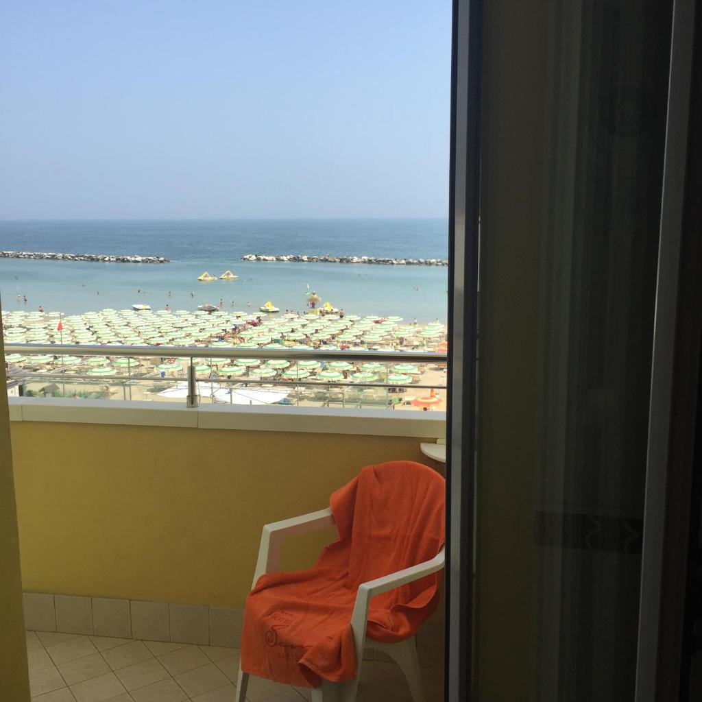 une chaise avec une serviette orange assise sur un balcon avec une plage dans l'établissement Hotel Sandra, à Gatteo a Mare