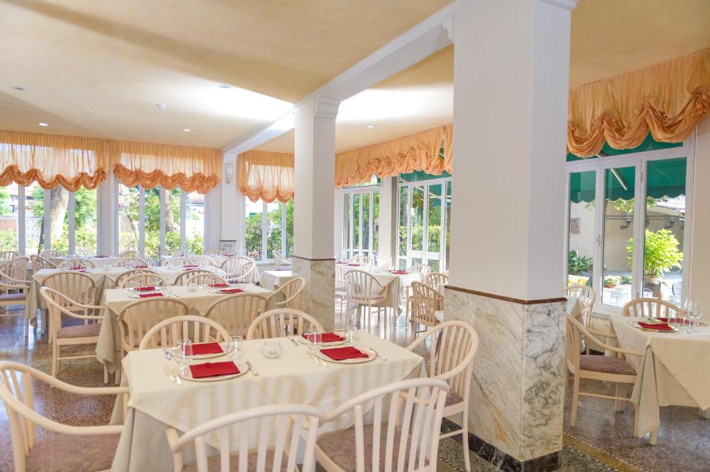 un restaurant avec des tables et des chaises blanches et des fenêtres dans l'établissement Albergo Battelli Only Adults, à Marina di Pietrasanta