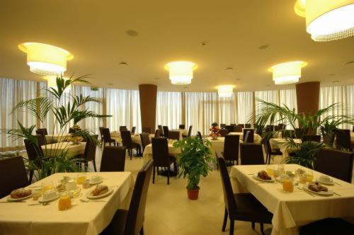 un restaurant avec des tables blanches, des chaises et des plantes dans l'établissement Mediterraneo Palace Hotel, à Amantea