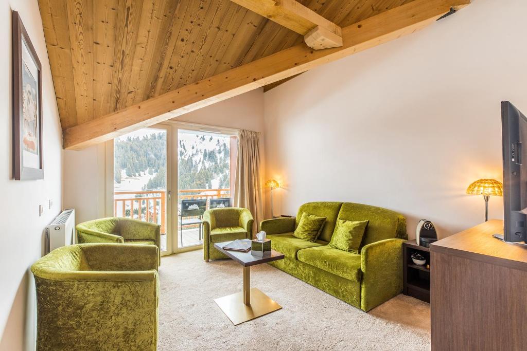 un salon avec deux chaises vertes et une télévision dans l'établissement Madame Vacances Hôtel & Spa Le Mottaret, à Méribel