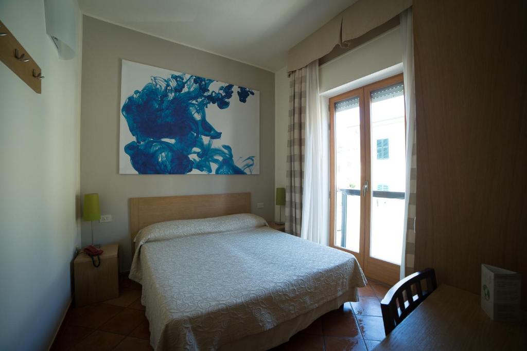 - une chambre avec un lit et un tableau bleu sur le mur dans l'établissement Hotel Miramare, à Castiglione della Pescaia