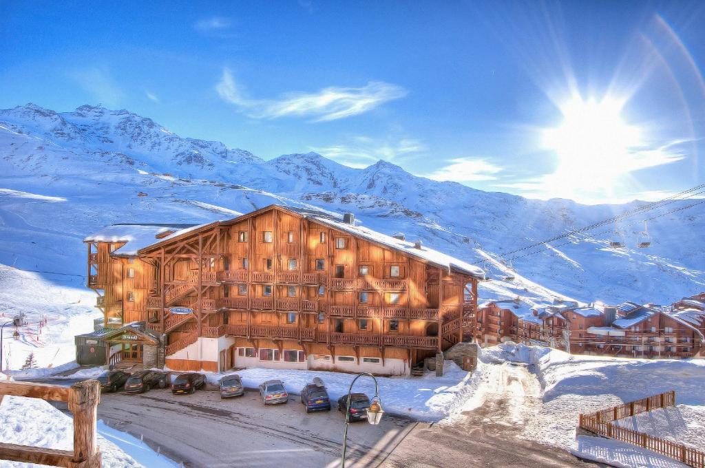 un grand bâtiment en bois dans la neige avec des montagnes dans l'établissement Résidence Les Balcons de Val Chavière, à Val Thorens
