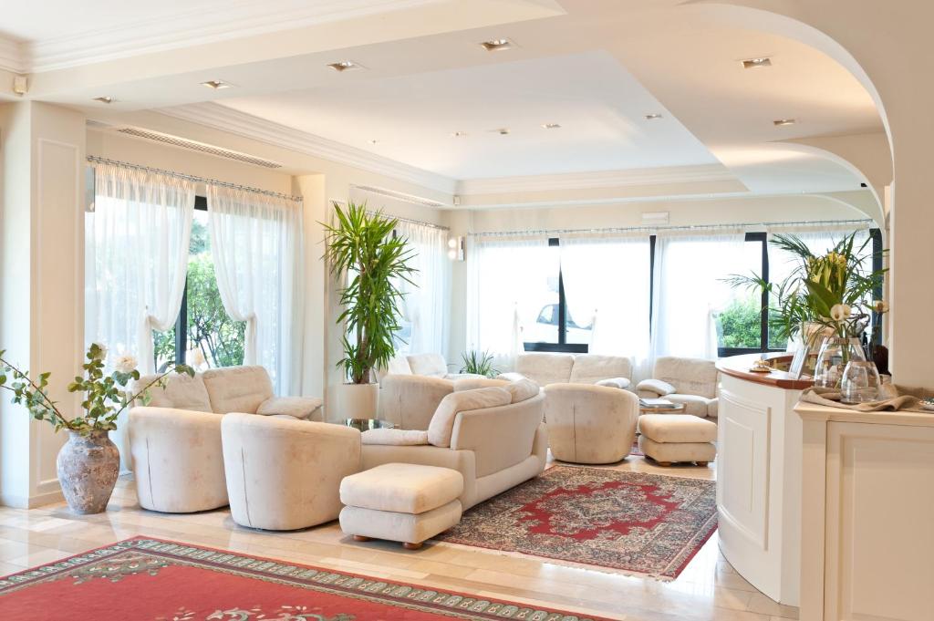un salon avec des meubles blancs et de grandes fenêtres dans l'établissement Hotel Derby Exclusive, à Milano Marittima