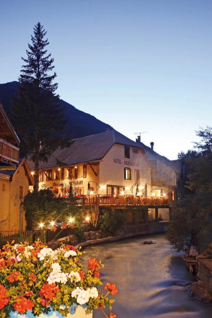 un bâtiment avec des lumières et des fleurs devant lui dans l'établissement Logis Hôtel et Spa Le Christiania, à La Salle Les Alpes