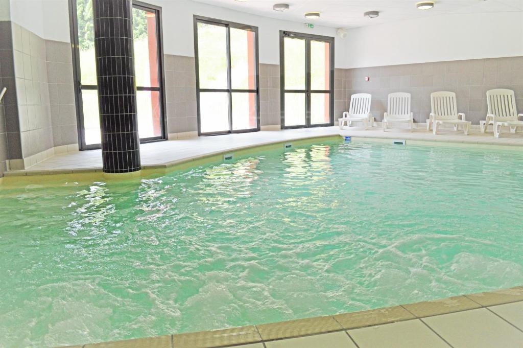 - une grande piscine avec des chaises blanches dans un bâtiment dans l'établissement Village club de Bois d'Amont, à Bois-dʼAmont