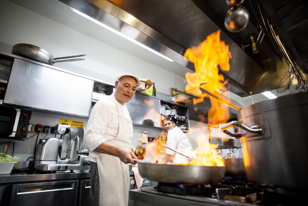 un chef préparant de la nourriture dans une cuisine avec des flammes dans l'établissement Hotel Majestic, à Milano Marittima