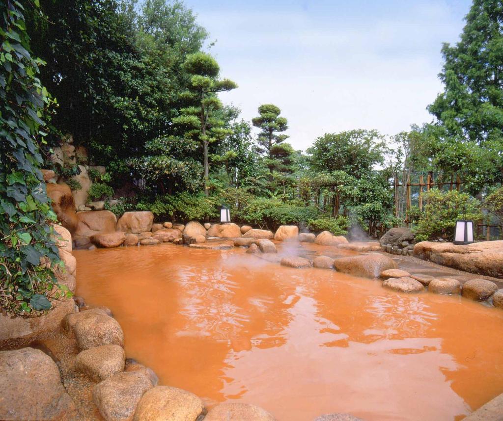 un bassin d'eau brune avec des rochers et des arbres dans l'établissement Hyoe Koyokaku, à Kobe