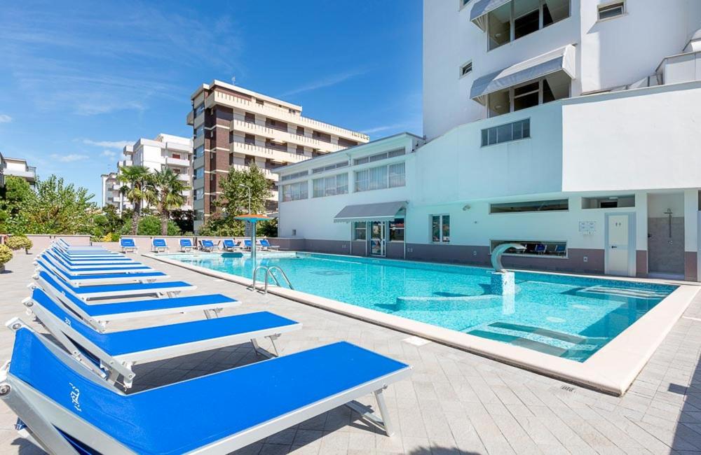 - une piscine avec des chaises longues bleues à côté d'un bâtiment dans l'établissement Hotel Excelsior, à Alba Adriatica