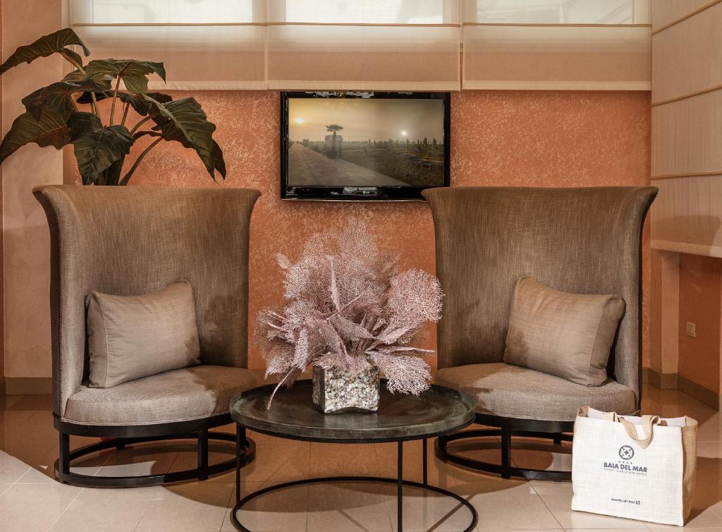 2 chaises et une table avec une télévision murale dans l'établissement Baia del Mar Beach Boutique Hotel, à Lido di Jesolo