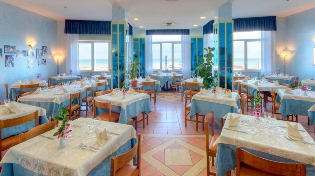 un restaurant avec des tables et des chaises blanches et des fenêtres dans l'établissement Hotel Giannino, à Porto Recanati