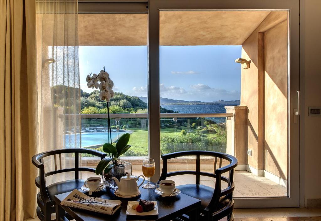 une table avec deux chaises devant une grande fenêtre dans l'établissement L'Ea Bianca Luxury Resort, à Baja Sardinia
