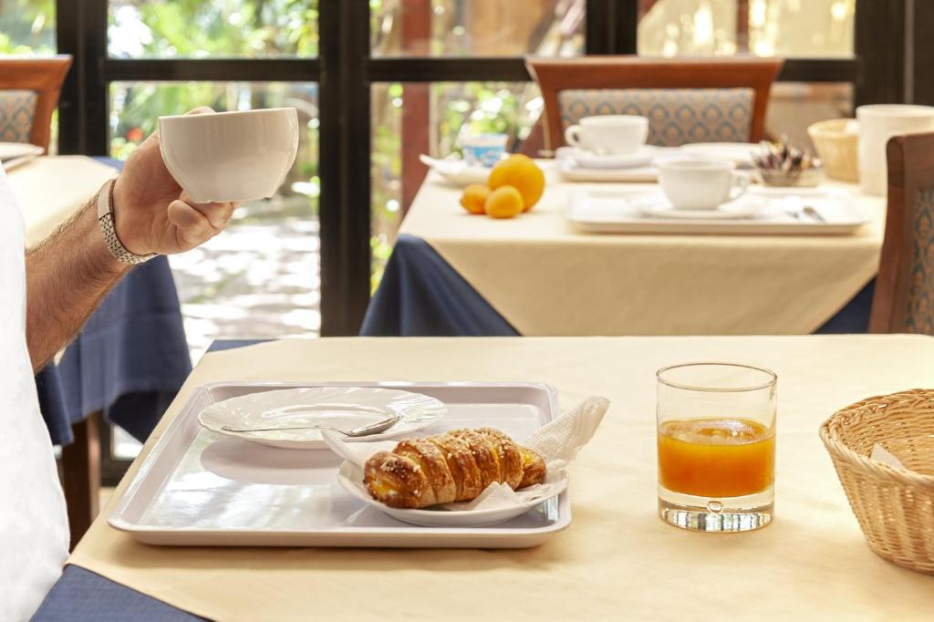 une personne tenant une tasse de café et une assiette de nourriture dans l'établissement Hotel Villa Lo Scoglietto, à San Vincenzo