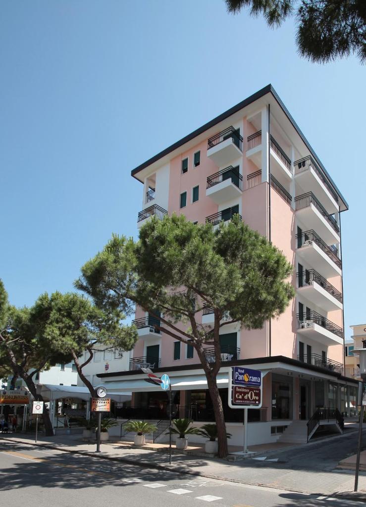 un grand bâtiment rose avec des arbres devant lui dans l'établissement Hotel Panorama, à Lido di Jesolo