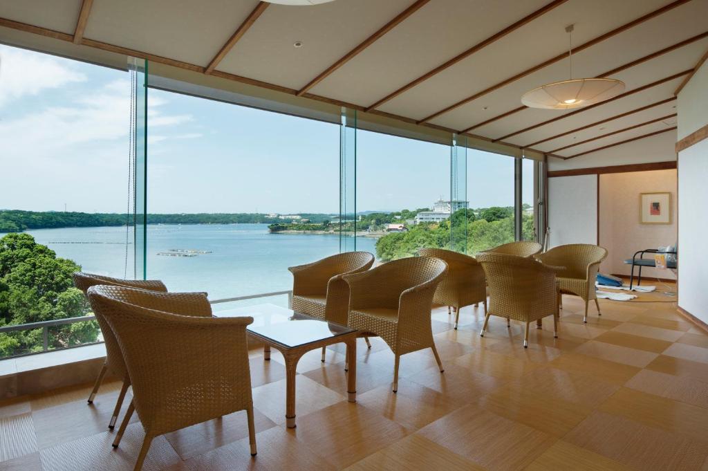 un groupe de chaises et de tables dans une pièce avec de grandes fenêtres dans l'établissement Kashikojima Hojoen, à Shima
